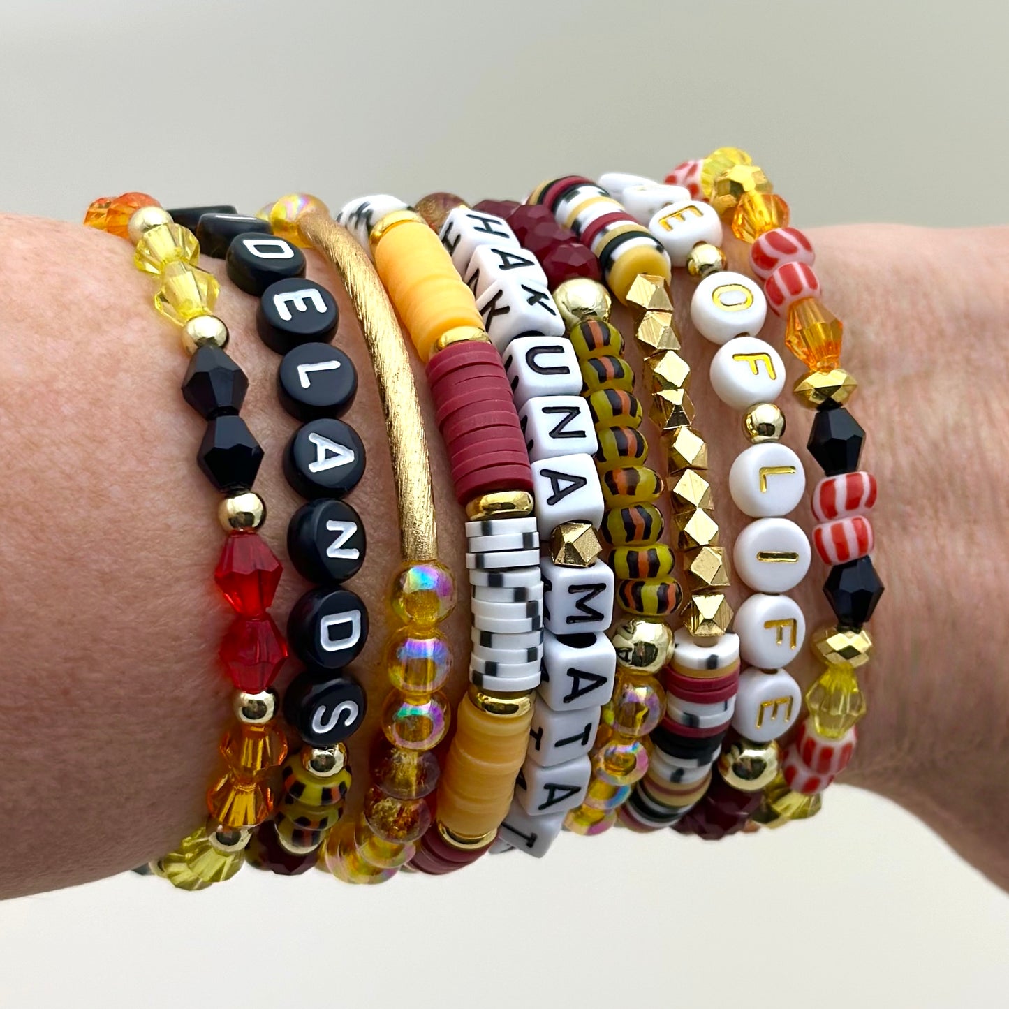 Broadway Stacks SAFARI collection. 3 stretch bracelets included in Stack. Dark reds, yellow, orange, white, black and gold colored beads. Animal print beads as well. Letter beads that spell Hakuna Matata.