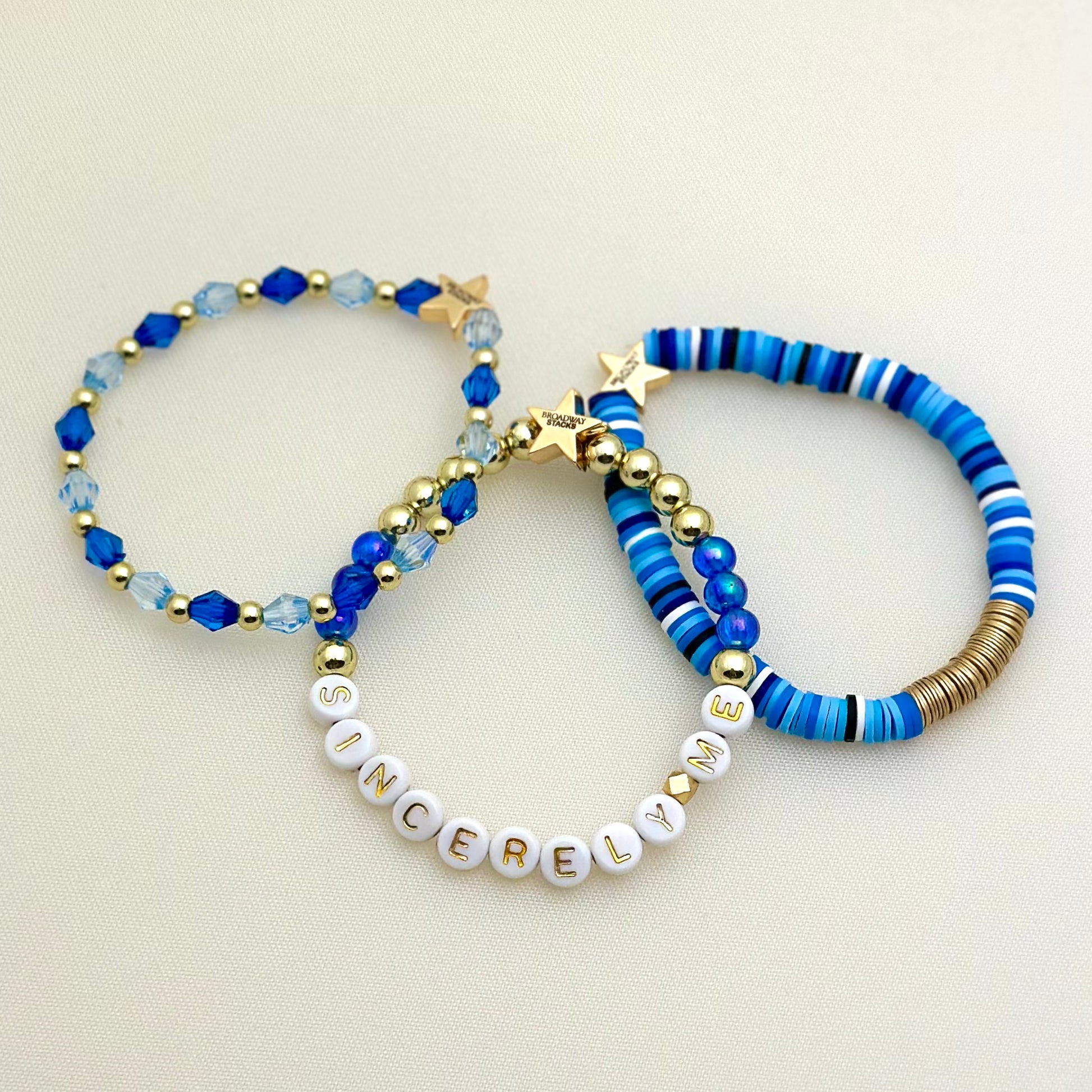 Broadway Stacks SKY collection. 3 stretch bracelets included in Stack. Blues, white, black and gold colored beads. Letter beads that spell Sincerely Me.