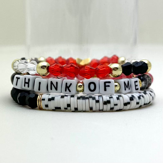 Broadway Stacks Phantom collection. 3 stretch bracelets included in Stack. Red, black, white and gold colored beads. Letter beads that spell Think Of Me.