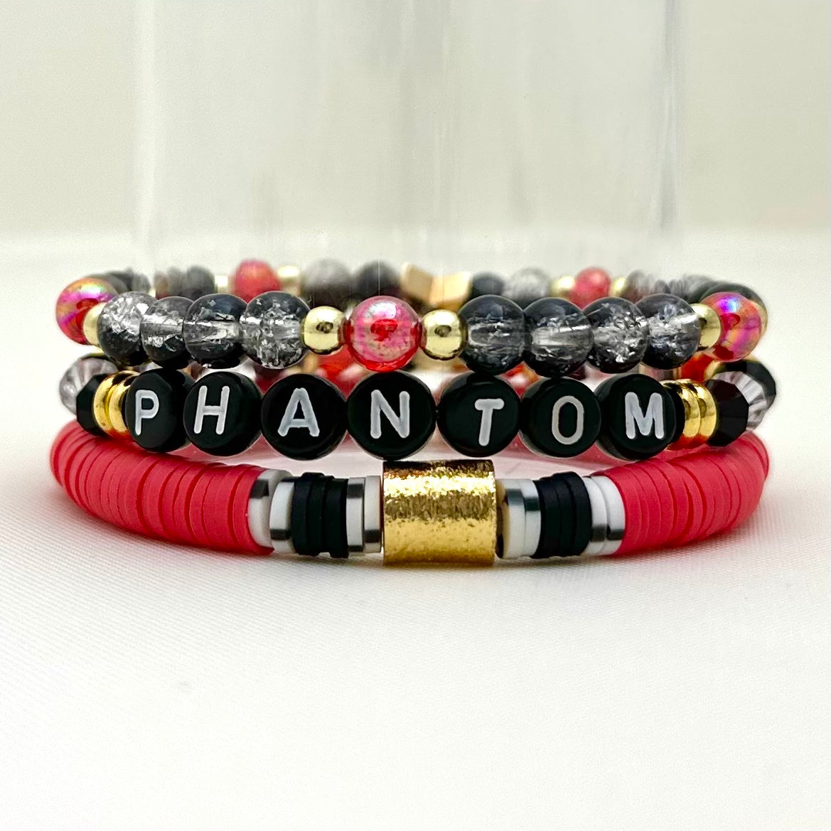 Broadway Stacks Phantom collection. 3 stretch bracelets included in Stack. Red, black, white and gold colored beads. Letter beads that spell Phantom.