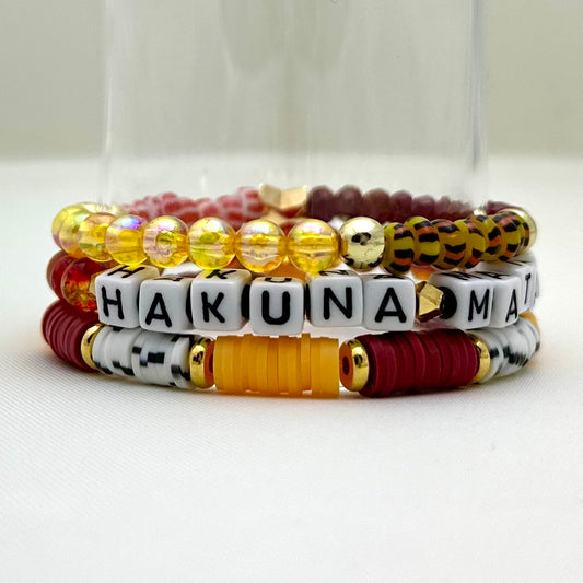 Broadway Stacks SAFARI collection. 3 stretch bracelets included in Stack. Dark reds, yellow, orange, white, black and gold colored beads. Animal print beads as well. Letter beads that spell Hakuna Matata.