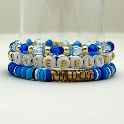 Broadway Stacks SKY collection. 3 stretch bracelets included in Stack. Blues, white, clear, gold and black colored beads. Letter beads that spell show quotes. Broadway Stacks gold star logo bead on back.