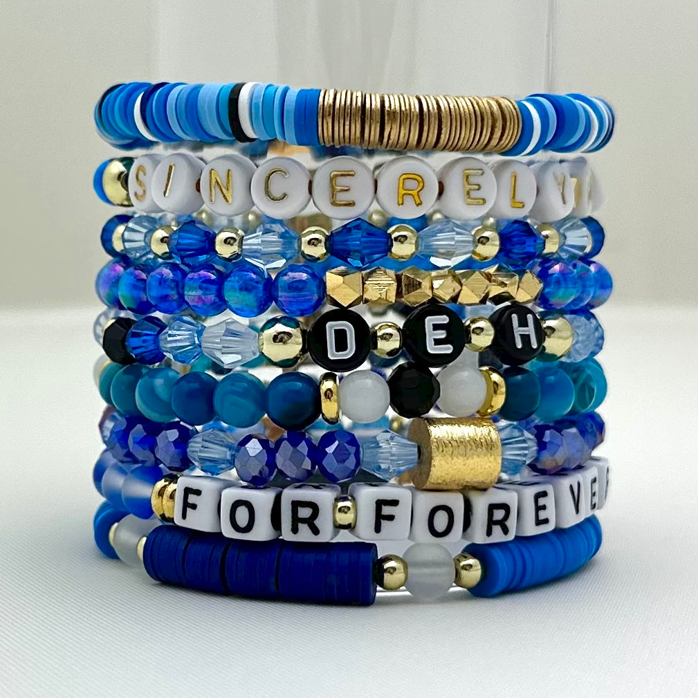 Broadway Stacks SKY collection. 3 stretch bracelets included in Stack. Blues, white, black and gold colored beads. Letter beads that spell DEH.