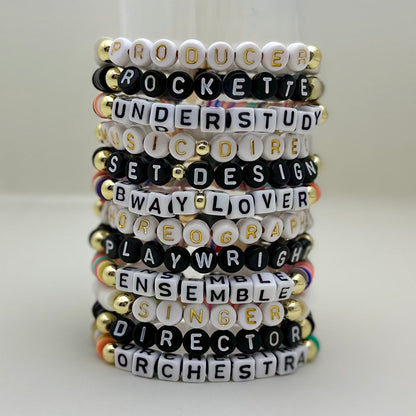 Broadway Stacks SPOTLIGHT Collection. Handcrafted beaded elastic-stretch bracelet with letter beads. Available in many varieties of theatre positions like actor, singer, dancer, director, stage manager, understudy, bway lover, crew, musician, etc. Gold color accents. Available in black, white and mulit-color. Broadway Stacks gold star logo bead on back.