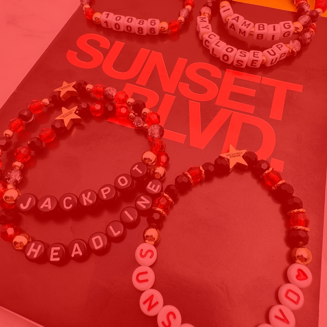 Broadway Stacks CLOSE-UP Collection. 6 stretch bracelets included in Stack. Red, black and gold colored beads. Letter beads that spell quotes. Gold star logo bead to remind you that you shine. Sunset Blvd fans. 