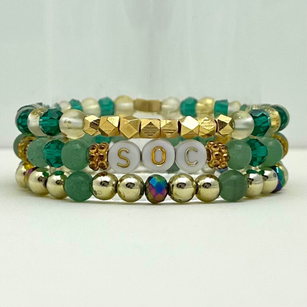 Broadway Stacks STAY GOLD collection. Stretch bracelets included in Stack. Gold, yellow, green and grey colored beads. Letter beads that have show quote or name. Broadway Stacks gold star logo bead on back.