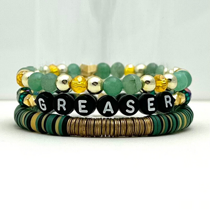 Broadway Stacks STAY GOLD collection. Stretch bracelets included in Stack. Gold, yellow, green and grey colored beads. Letter beads that have show quote or name. Broadway Stacks gold star logo bead on back.