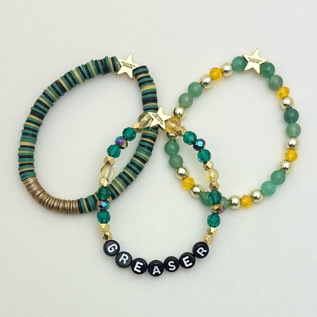 Broadway Stacks STAY GOLD collection. Stretch bracelets included in Stack. Gold, yellow, green and grey colored beads. Letter beads that have show quote or name. Broadway Stacks gold star logo bead on back.