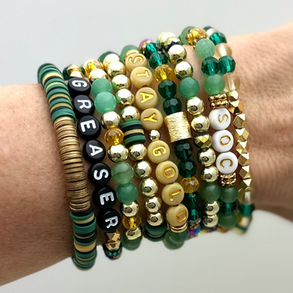 Broadway Stacks STAY GOLD collection. Stretch bracelets included in Stack. Gold, yellow, green and grey colored beads. Letter beads that have show quote or name. Broadway Stacks gold star logo bead on back.