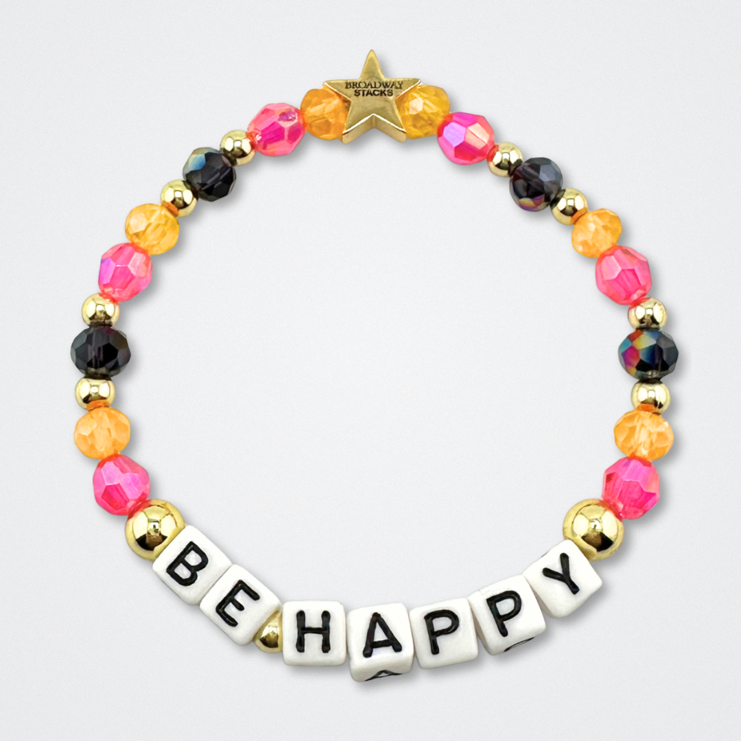 Broadway Stacks CAKE Collection. Be Happy bracelet with yellow, pink black and gold colored beads. Letter beads that spell quote. Star logo bead to remind you that you shine. Two Strangers Carry a Cake Across New York fans.