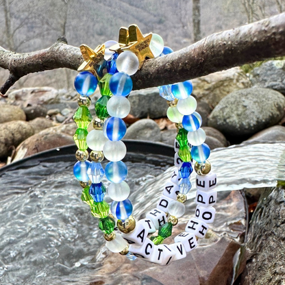 Earth Day Special Edition bracelet. Stack of 3 bracelets. Green, blue, white and gold beads. Letter beads that spell Earth Day 25 and Active Hope. Gold star logo bead to remind you that You Shine.