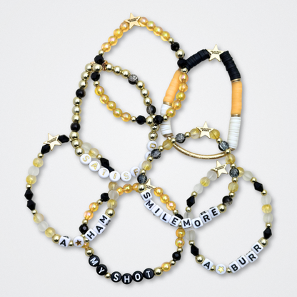 Broadway Stacks REVOLUTION Collection. 5 stretch bracelets included in Stack. Yellow, white, black and gold colored beads. Letter beads that spell quotes. Gold star logo bead to remind you that You Shine. Hamilton the Musical fans. 