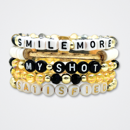 Broadway Stacks REVOLUTION Collection. 5 stretch bracelets included in Stack. Yellow, white, black and gold colored beads. Letter beads that spell quotes. Gold star logo bead to remind you that You Shine. Hamilton the Musical fans. 