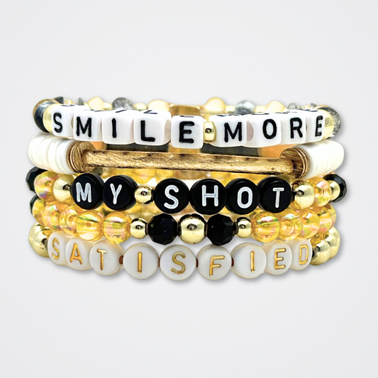 Broadway Stacks REVOLUTION Collection. 5 stretch bracelets included in Stack. Yellow, white, black and gold colored beads. Letter beads that spell quotes. Gold star logo bead to remind you that You Shine. Hamilton the Musical fans. 