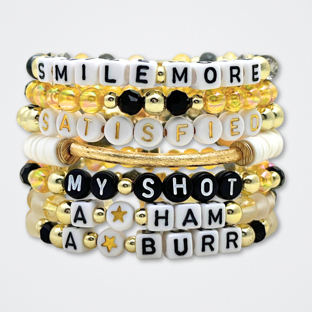 Broadway Stacks REVOLUTION Collection. 5 stretch bracelets included in Stack. Yellow, white, black and gold colored beads. Letter beads that spell quotes. Gold star logo bead to remind you that You Shine. Hamilton the Musical fans. 