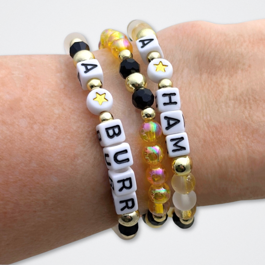 Broadway Stacks REVOLUTION Collection. 5 stretch bracelets included in Stack. Yellow, white, black and gold colored beads. Letter beads that spell quotes. Gold star logo bead to remind you that You Shine. Hamilton the Musical fans. 