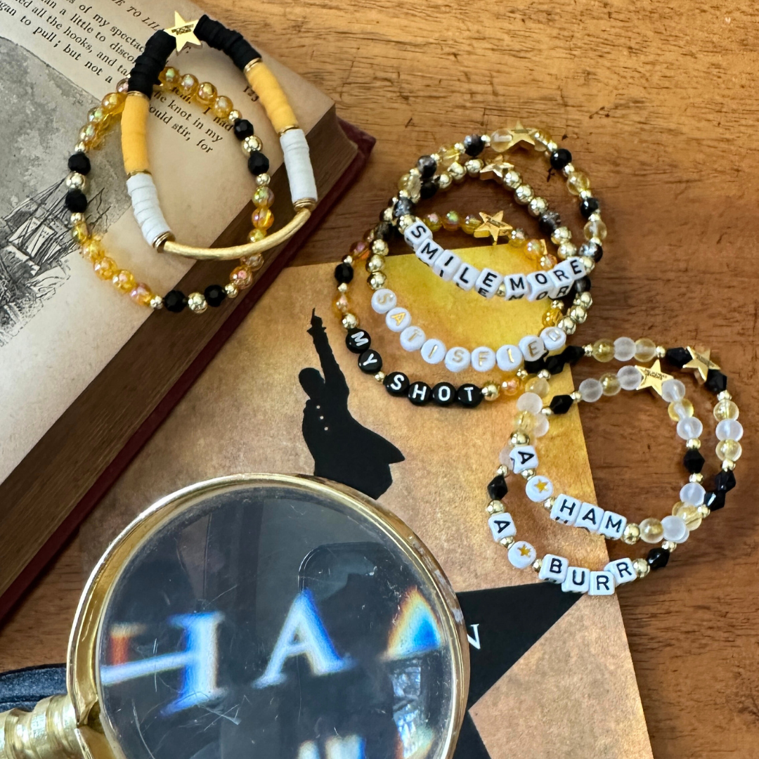 Broadway Stacks REVOLUTION Collection. 5 stretch bracelets included in Stack. Yellow, white, black and gold colored beads. Letter beads that spell quotes. Gold star logo bead to remind you that You Shine. Hamilton the Musical fans. 