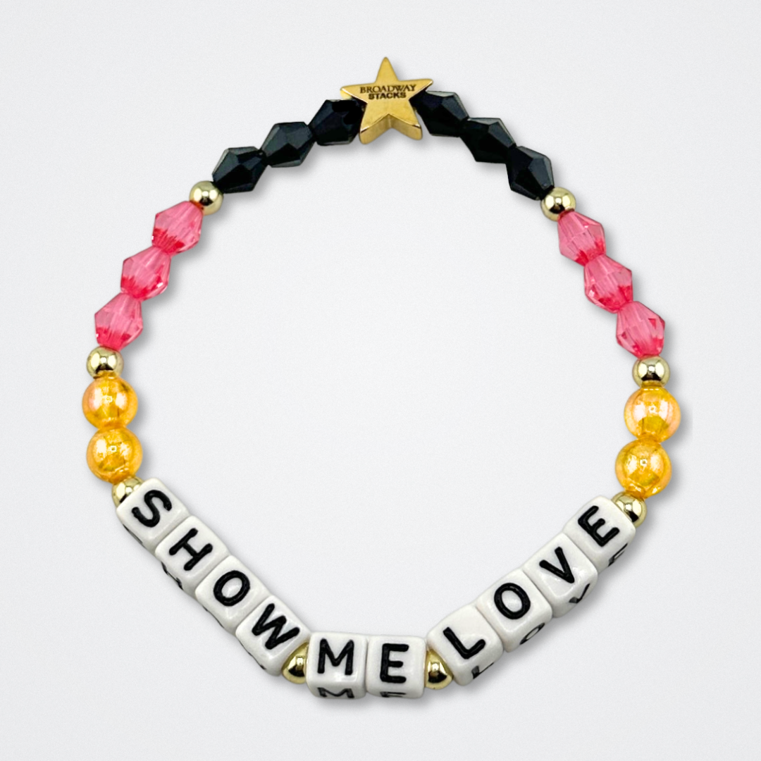 Broadway Stacks De Bois Band collection. Pink, yellow, gold and black colored beads on bracelet on gray background. Letter beads that spell quotes. Broadway Stacks gold star logo bead to remind you that you shine. & Juliet the Musical fans.