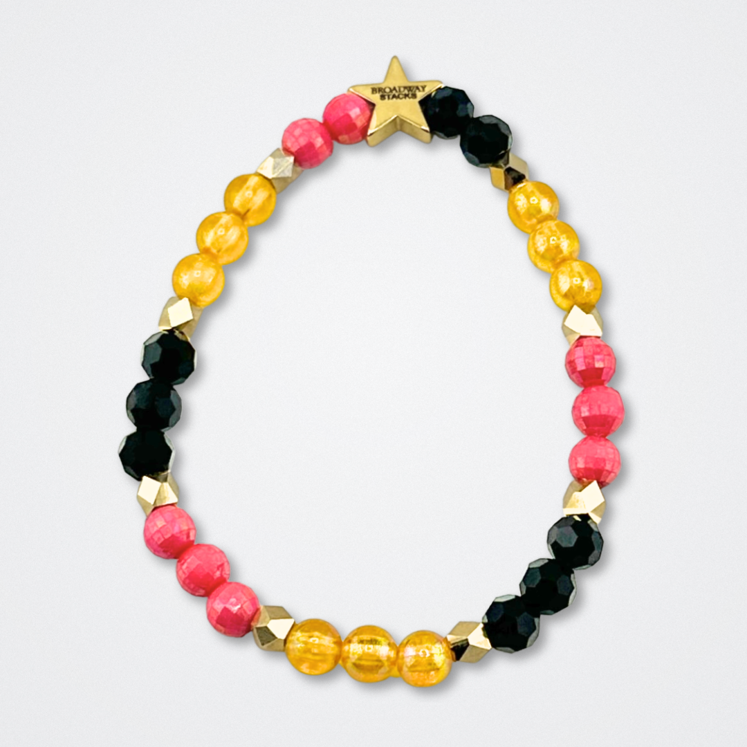 Broadway Stacks De Bois Band collection. Pink, yellow, gold and black colored beads on bracelet on gray background. Broadway Stacks gold star logo bead to remind you that you shine. & Juliet the Musical fans.