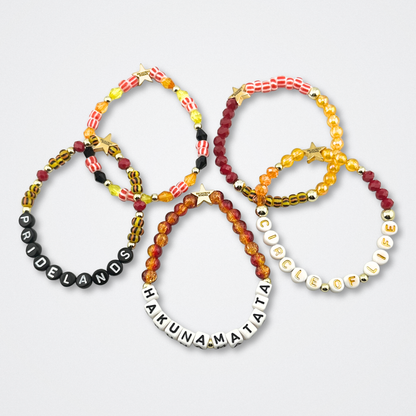 Broadway Stacks SAFARI collection.Yellow, orange, red, black, animal print and gold colored beads on bracelets on gray background. Star logo bead to remind you that YOU SHINE! The Lion King and theatre fans.