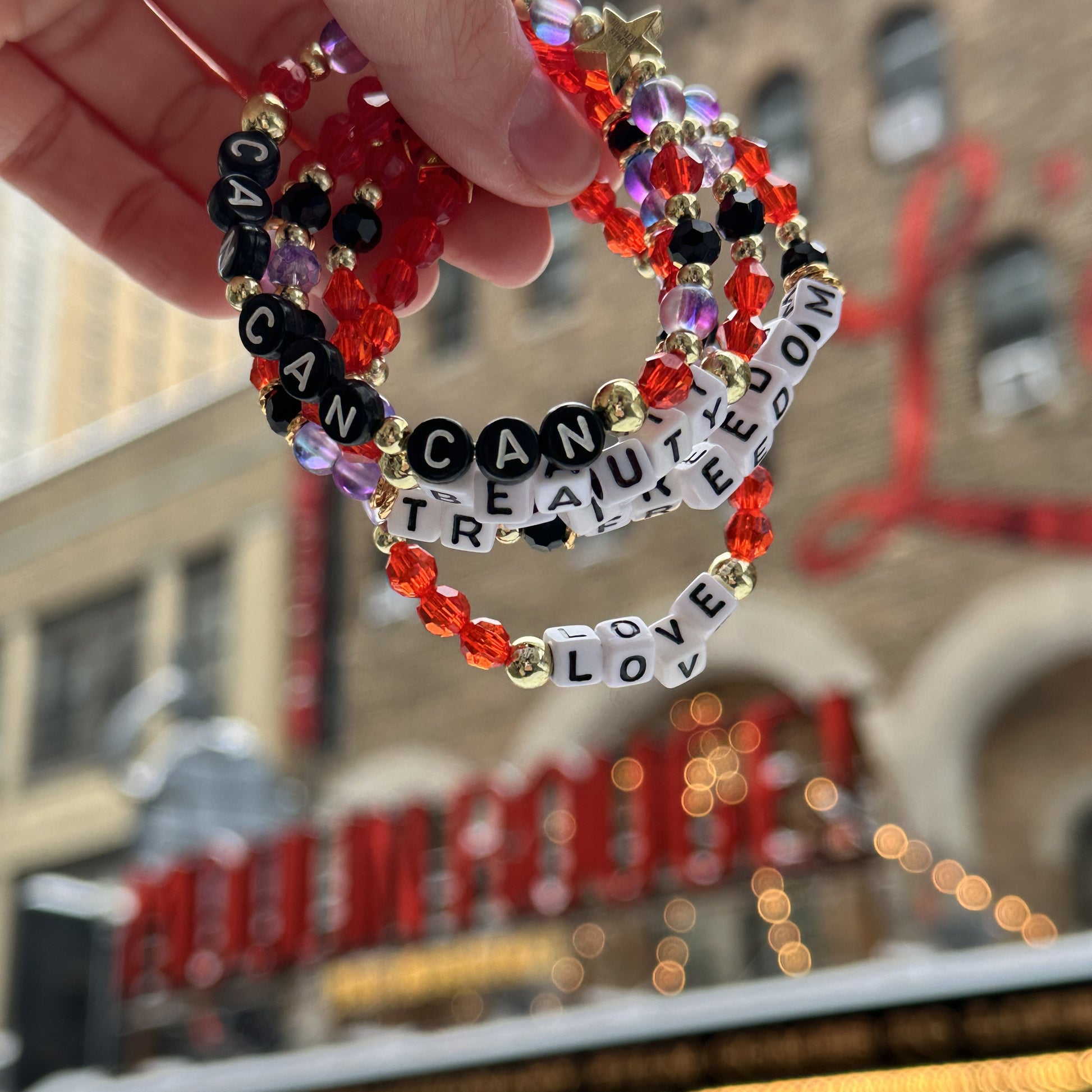 Broadway Stacks RED LIGHT bracelets being held in front of theatre marquee for Moulin Rouge, Al Hirschfeld Theatre