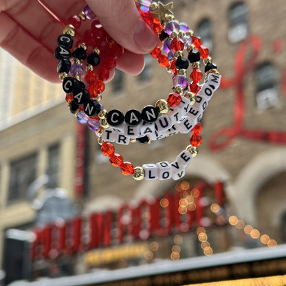 Broadway Stacks RED LIGHT bracelets being held in front of theatre marquee for Moulin Rouge, Al Hirschfeld Theatre