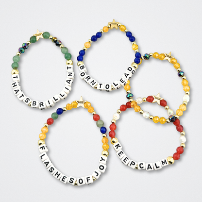 Broadway Stacks CONFIDENTIAL Collection. 5 stretch bracelets laid flat. Black, white, red, blue, green, yellow and gold colored beads. Letter beads that spell quotes. Star logo bead to remind you that you shine. Operation Mincemeat fans.