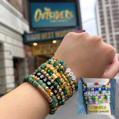 Broadway Stacks STAY GOLD collection. Stretch bracelets included in Stack. Gold, yellow, green and grey colored beads. Letter beads that have show quote or name. Broadway Stacks gold star logo bead to remind you that You Shine. The Outsiders the Musical fans.