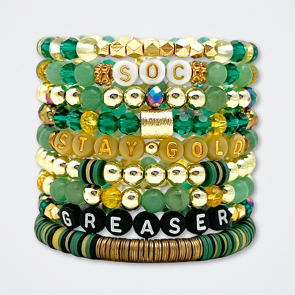 Broadway Stacks STAY GOLD collection. Stretch bracelets included in Stack. Gold, yellow, green and grey colored beads. Letter beads that have show quote or name. Broadway Stacks gold star logo bead to remind you that You Shine. The Outsiders the Musical fans.