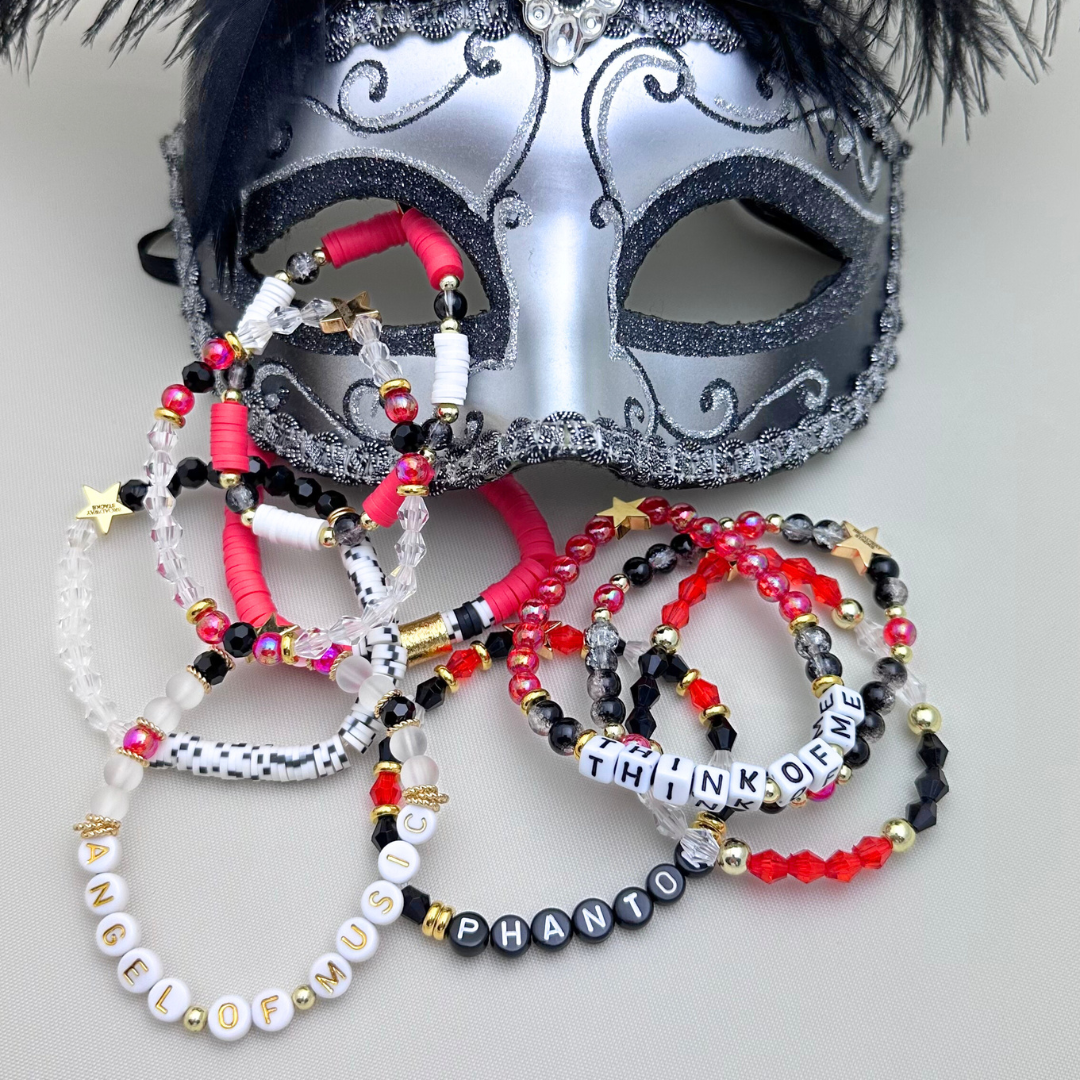 Broadway Stacks MASK collection. Bead bracelets included in Stack. Red, black, white and gold colored beads. Letter beads that spell quotes. Team Phantom, Team Christine, Team Raoul. Gold star logo bead to remind you that You Shine. Phantom of the Opera and Masquerade fans.