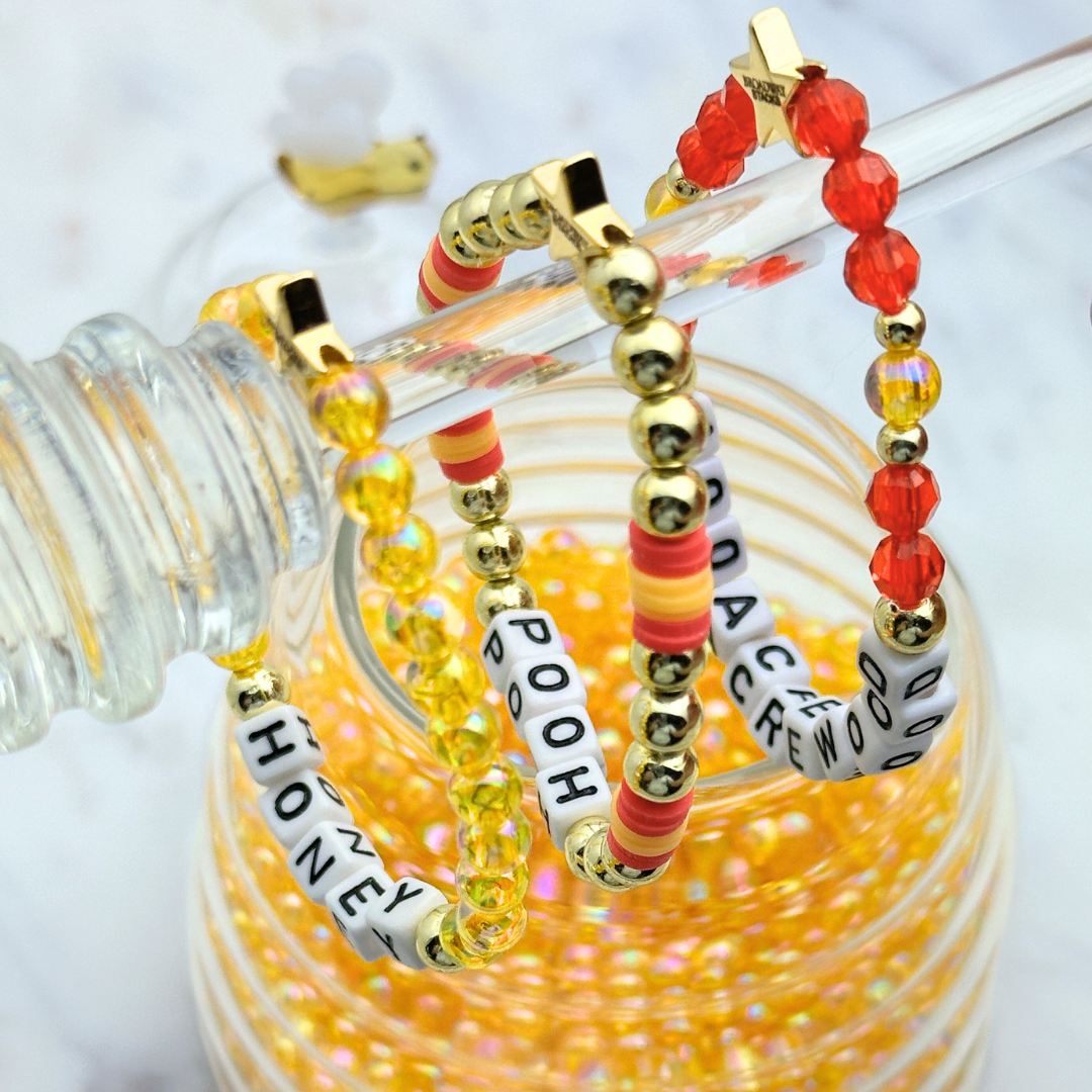Broadway Stacks HONEY Collection. 3 stretch bracelets included in Stack. Red, yellow and gold colored beads. Letter beads that spell quotes. Gold star logo bead to remind you that You Shine. Winnie the Pooh fans.