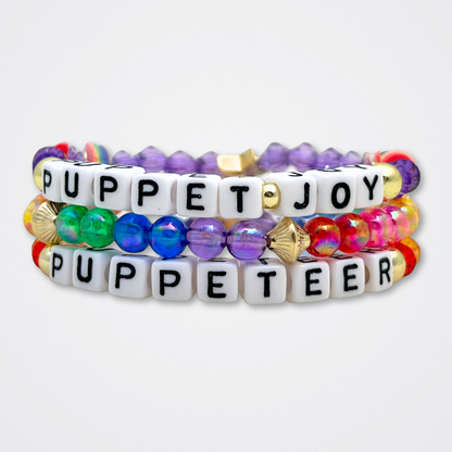 Broadway Stacks PUPPETRY Collection Special Edition bracelet. Stack of 3 bracelets. Rainbow and gold beads. Letter beads that spell Puppeteer and Puppet Joy. Gold star logo bead to remind you that You Shine. 