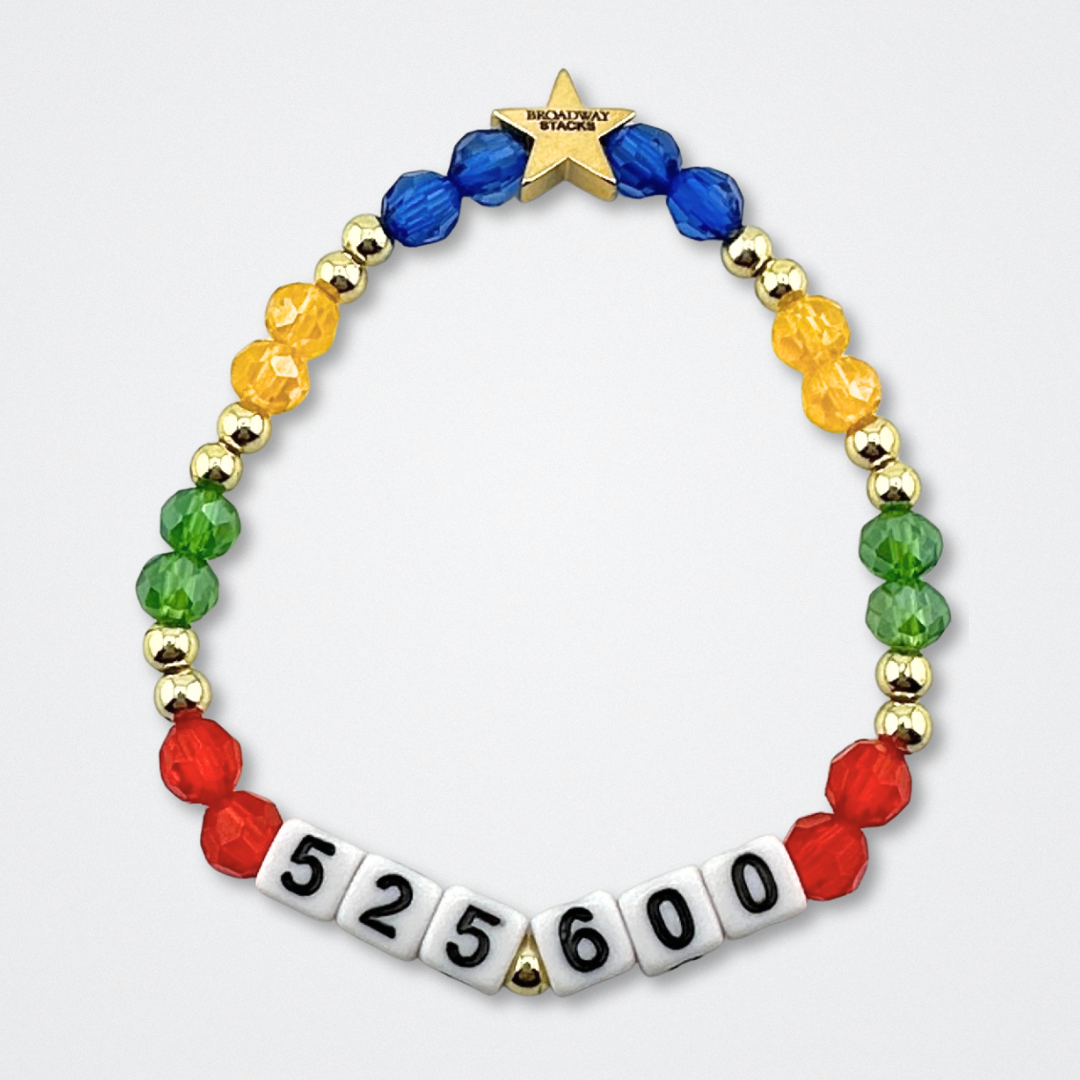 Broadway Stacks theatre-themed bracelet inspired by RENT the Musical. Quote says 525,600 with red, green, yellow and blue beads on a gray background. Signature star bead to remind you that You Shine!