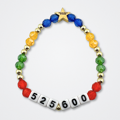 Broadway Stacks theatre-themed bracelet inspired by RENT the Musical. Quote says 525,600 with red, green, yellow and blue beads on a gray background. Signature star bead to remind you that You Shine!