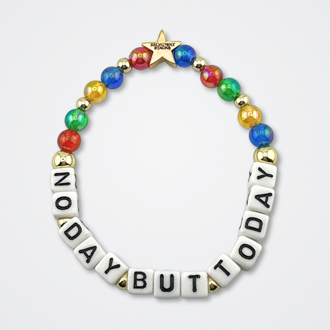 Broadway Stacks theatre-themed bracelet inspired by RENT the Musical. Quote says NO DAY BUT TODAY with red, green, yellow and blue beads on a gray background. Signature star bead to remind you that You Shine!