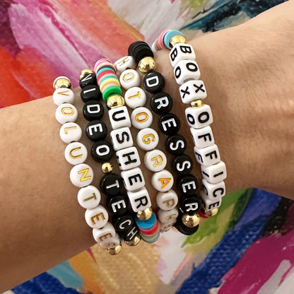 Bracelets with letter beads on a wrist against a colorful background. Broadway Stacks theatre-themed Spotlight bracelets highlighting ALL theater roles. Because everyone deserves to shine.