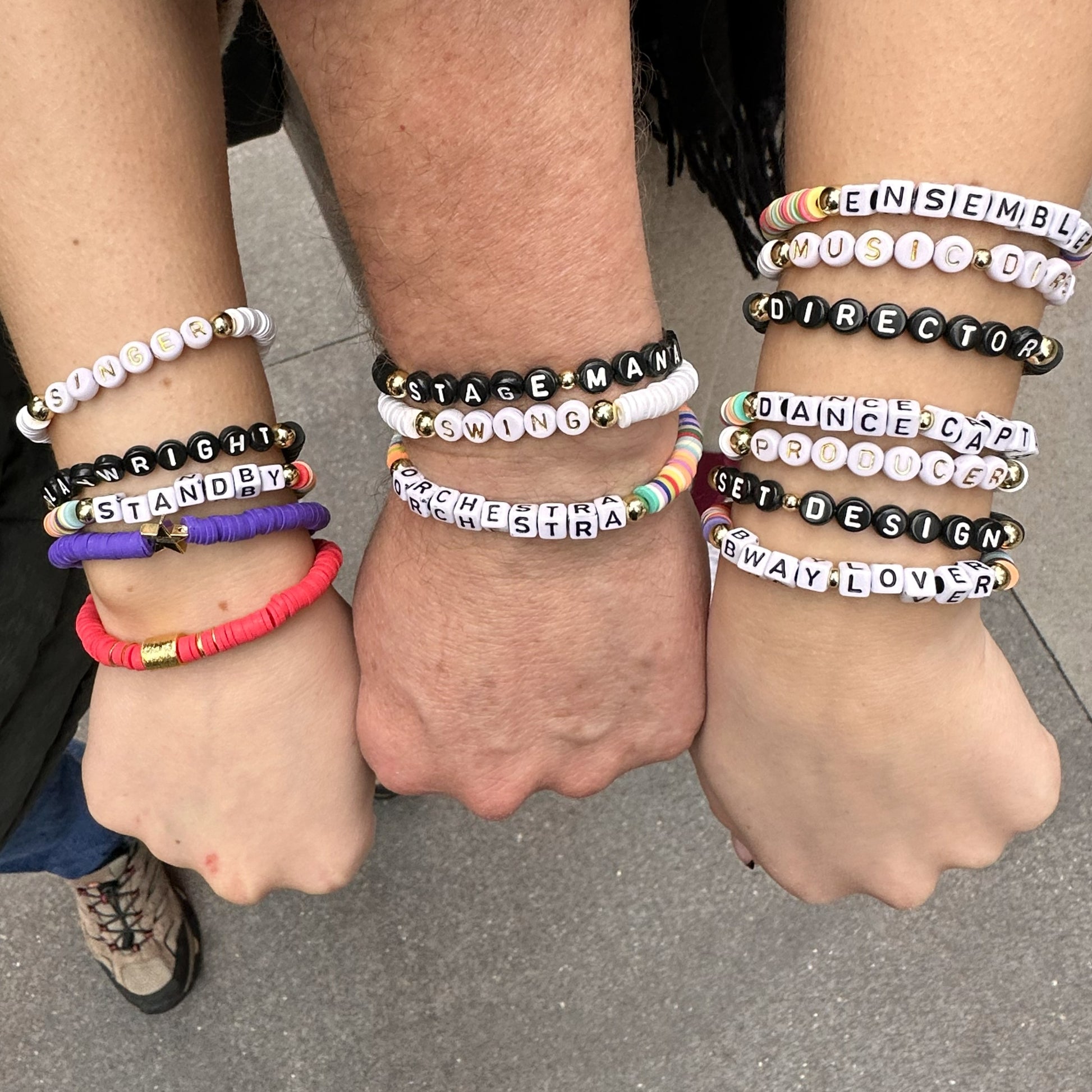 Three wrists wearing multiple bracelets with various text. Broadway Stacks theatre-themed Spotlight bracelets highlighting ALL theater roles. Because everyone deserves to shine.