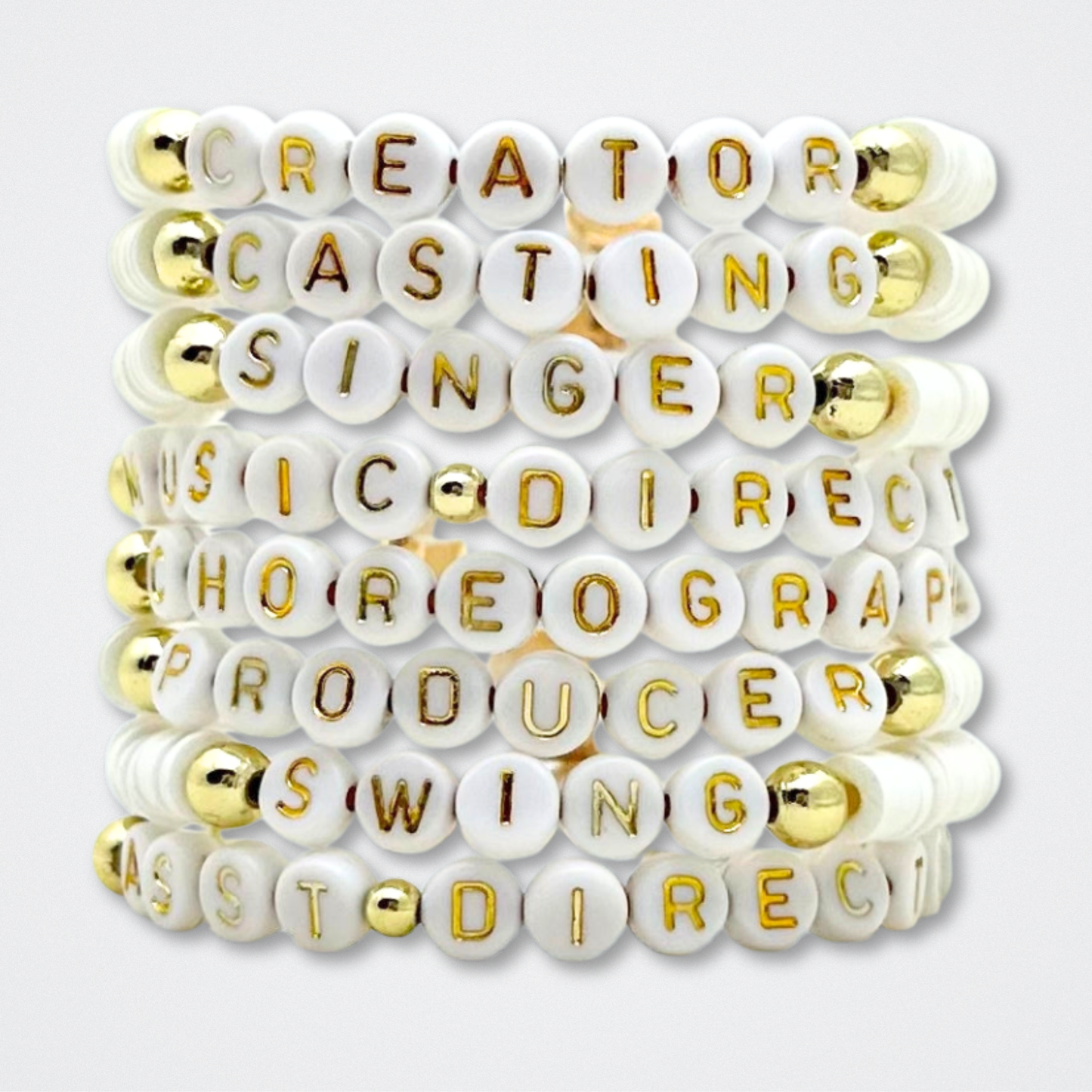 Bracelet with white beads featuring gold letters on a white background. Broadway Stacks theatre-themed Spotlight bracelets highlighting ALL theater roles. Because everyone deserves to shine.