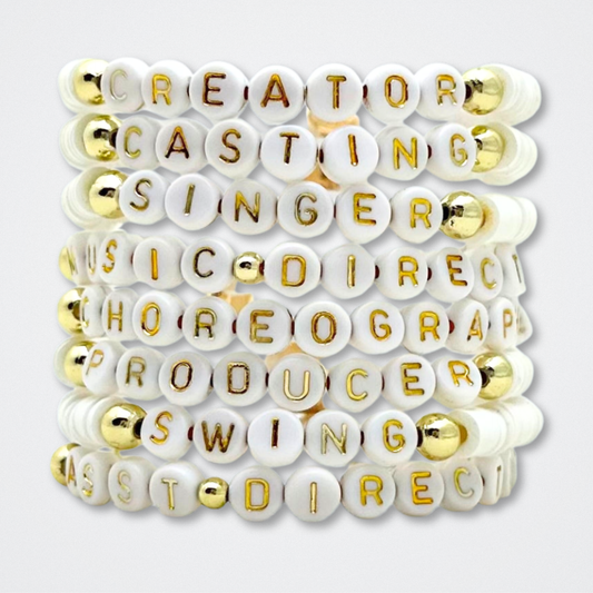Bracelet with white beads featuring gold letters on a white background. Broadway Stacks theatre-themed Spotlight bracelets highlighting ALL theater roles. Because everyone deserves to shine.