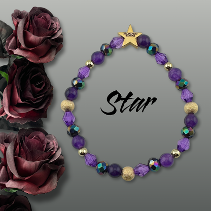 Variety of purple beads on bracelet on a dark gray background with burgundy roses on the side. Inspired by he character STAR in The Lost Boys Musical. Broadway Stacks VAMPIRE Collection. Gold star logo bead to remind you that you shine. 