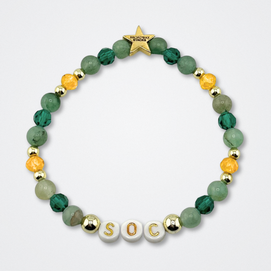 Broadway Stacks STAY GOLD bracelet inspired by The Outsiders Musical. Green and gold beads with letter beads that spell SOC. Logo star bead to remind you that YOU SHINE. Displayed on a gray background.