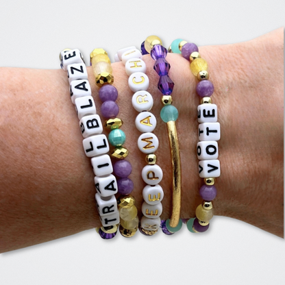 Broadway Stacks CAMPAIGN Collection. 5 stretch bracelets included in Stack. Purple, yellow, teal and gold colored beads. Letter beads that spell quotes. Gold star logo bead to remind you that you shine. Suffs fans. 
