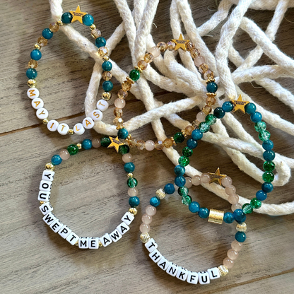 Broadway Stacks SAILOR Collection. 5 stretch bracelets included in Stack. Teal, green, blue and gold colored beads. Letter beads that spell quotes. Swept Away the Musical. Gold star logo bead to remind you that you shine.