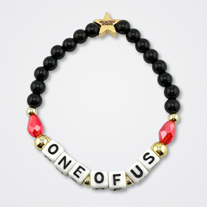 Bead bracelet with letter beads spelling 'ONE OF US' on a gray background. Broadway Stacks VAMPIRE Collection. Black, red and gold colored beads. Gold star logo bead to remind you that you shine. Inspired by The Lost Boys Musical.