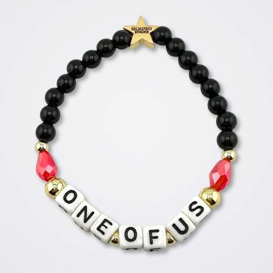 Bead bracelet with letter beads spelling 'ONE OF US' on a gray background. Broadway Stacks VAMPIRE Collection. Black, red and gold colored beads. Gold star logo bead to remind you that you shine. Inspired by The Lost Boys Musical.
