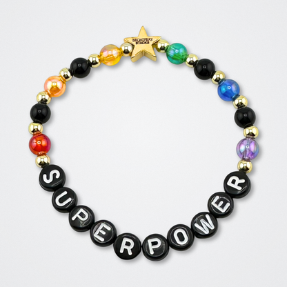 Bead bracelet with letter beads spelling 'SUPERPOWER' on a gray background. Broadway Stacks VAMPIRE Collection. Black,gold and rainbow colored beads. Gold star logo bead to remind you that you shine. Inspired by The Lost Boys Musical.
