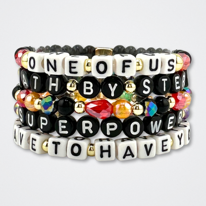 Broadway Stacks VAMPIRE Collection bead bracelets stacked on a gray background. Black, red, orange and gold colored beads with letter beads spelling out quotes. Inspired by The Lost Boys Musical.