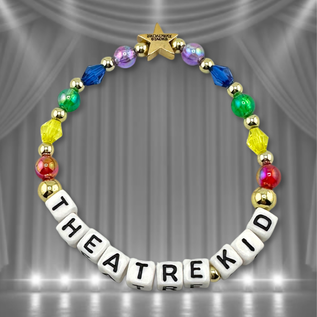 Broadway Stacks THEATRE KID rainbow bead bracelet displayed on a black/white stage curtain background. Letter beads spell out quote. Signature star bead to remind you: YOU SHINE! available. 