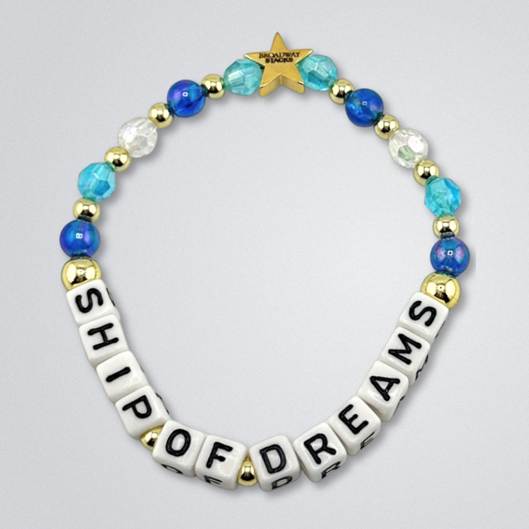 Bead bracelet with letter beads spelling 'SHIP OF DREAMS' on a gray background. Broadway Stacks UNSINKABLE Collection. Blues, clear and gold colored beads. Gold star logo bead to remind you that you shine. Inspired by Titanique the Musical.
