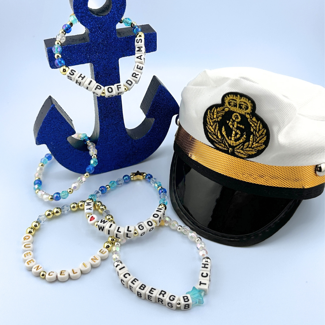 Nautical-themed accessories including a captain's hat, anchor, and beaded bracelets on a light blue background. Part of the Broadway Stacks UNSINKABLE Collection. Inspired by Titanique the Musical.